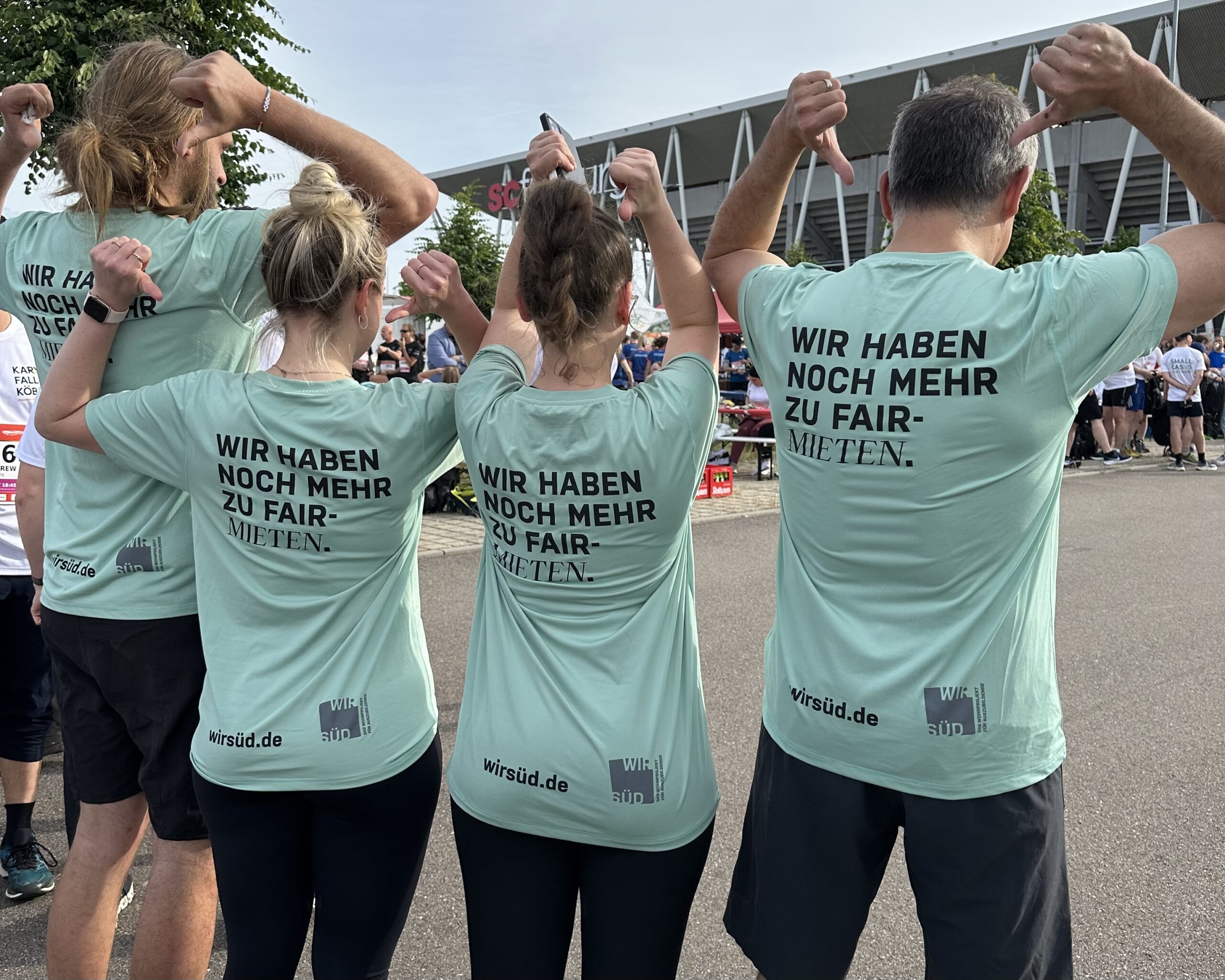 vier Personen, die auf die Rückseite ihres Shirts zeigen, mit der Aufschrift "WIR HABEN NOCH MEHR ZU FAIR-MIETEN"